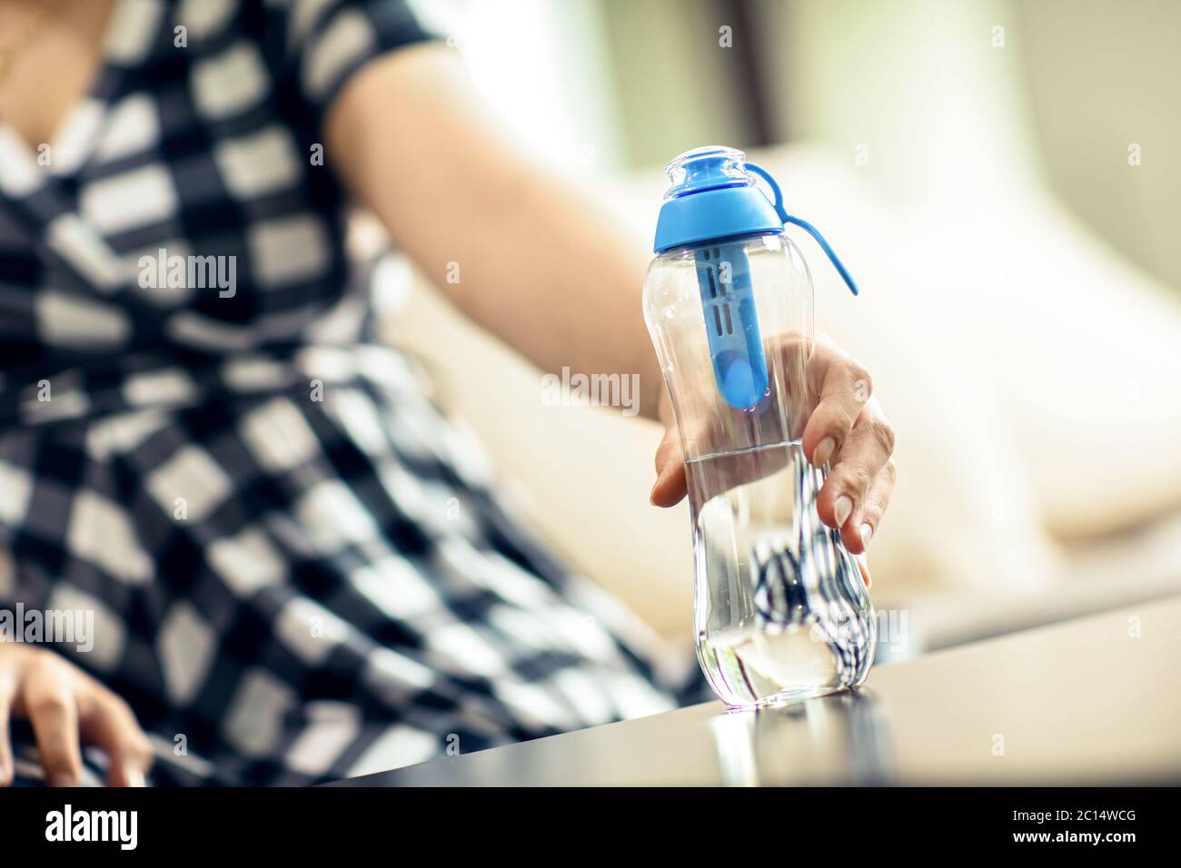 Frau greift die Flasche gefiltertes Wasser vom Tisch. Frau greift die wiederverwendbare Flasche mit Frischwasser mit Kohlefilter vom Tisch. Stockfoto