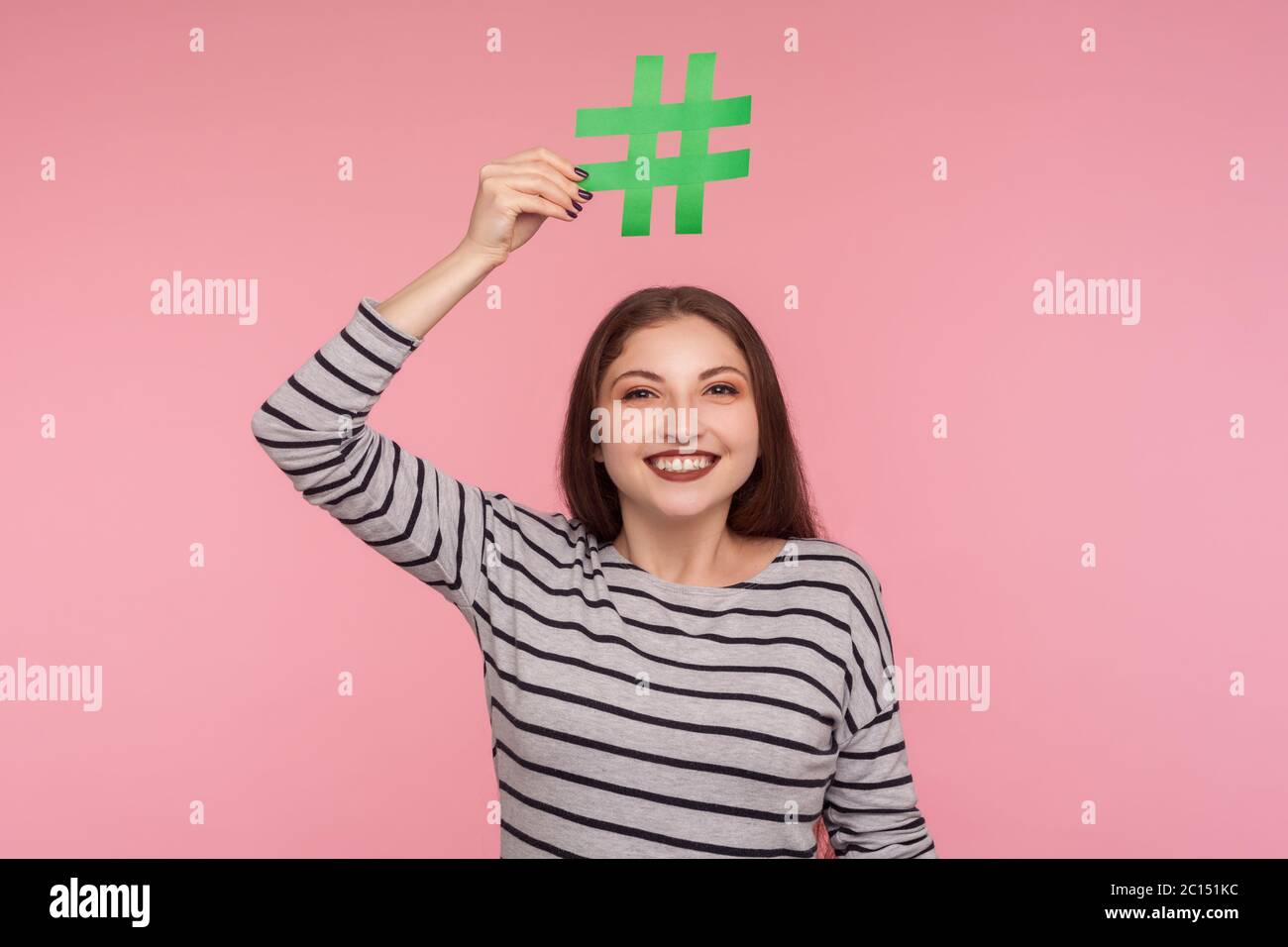 Überprüfen Sie virale Internet-Thema! Porträt von glücklichen jungen Frau in Sweatshirt Hashtag Symbol über dem Kopf und Blick auf die Kamera mit toothy Lächeln, folgenden tr Stockfoto