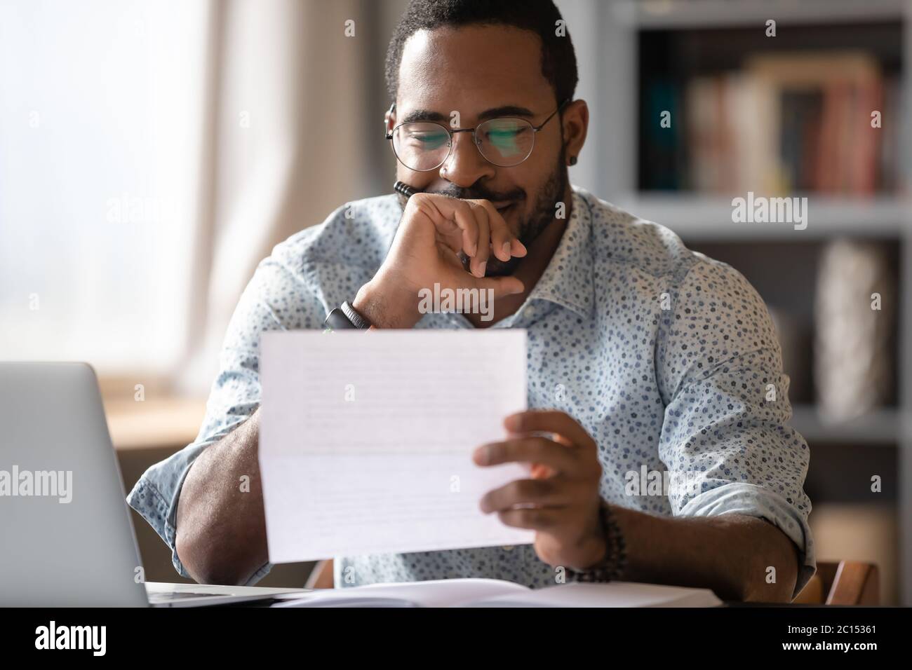 Der Afrikaner, der am Empfang sitzt und den Brief liest, fühlt sich zufrieden Stockfoto
