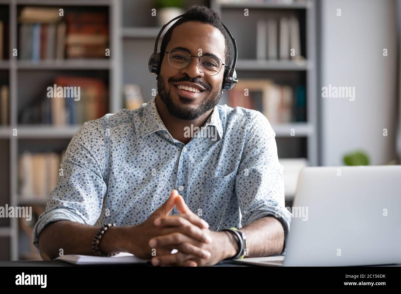 Afrikanischer Mann trägt ein Headset, das sich am Schreibtisch mit Blick auf die Kamera aufsetzt Stockfoto