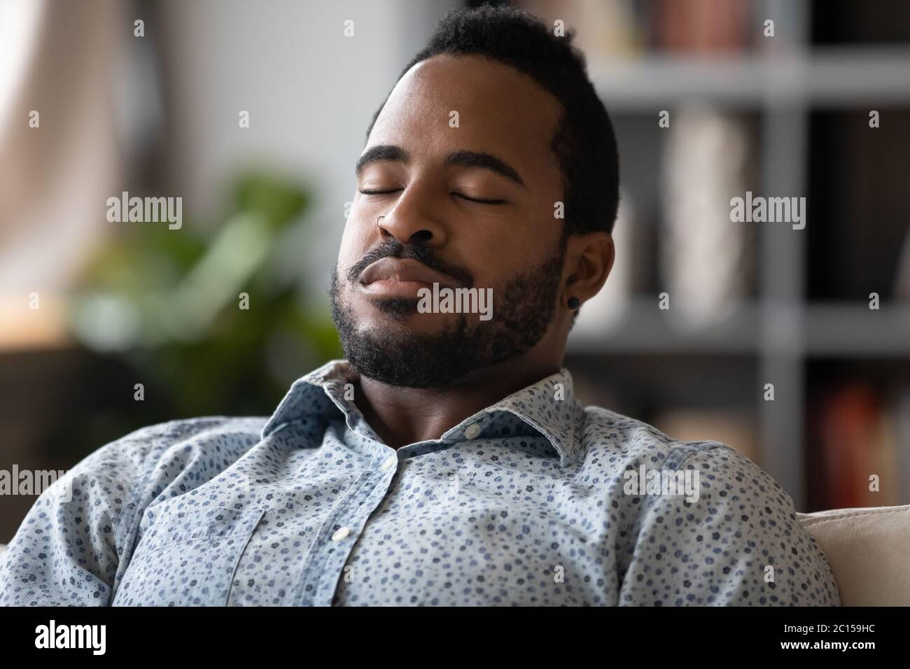 Nahaufnahme Afrikanischer junger Mann sitzt auf der Couch geschlossene Augen Ruhe reduziert Müdigkeit Stockfoto