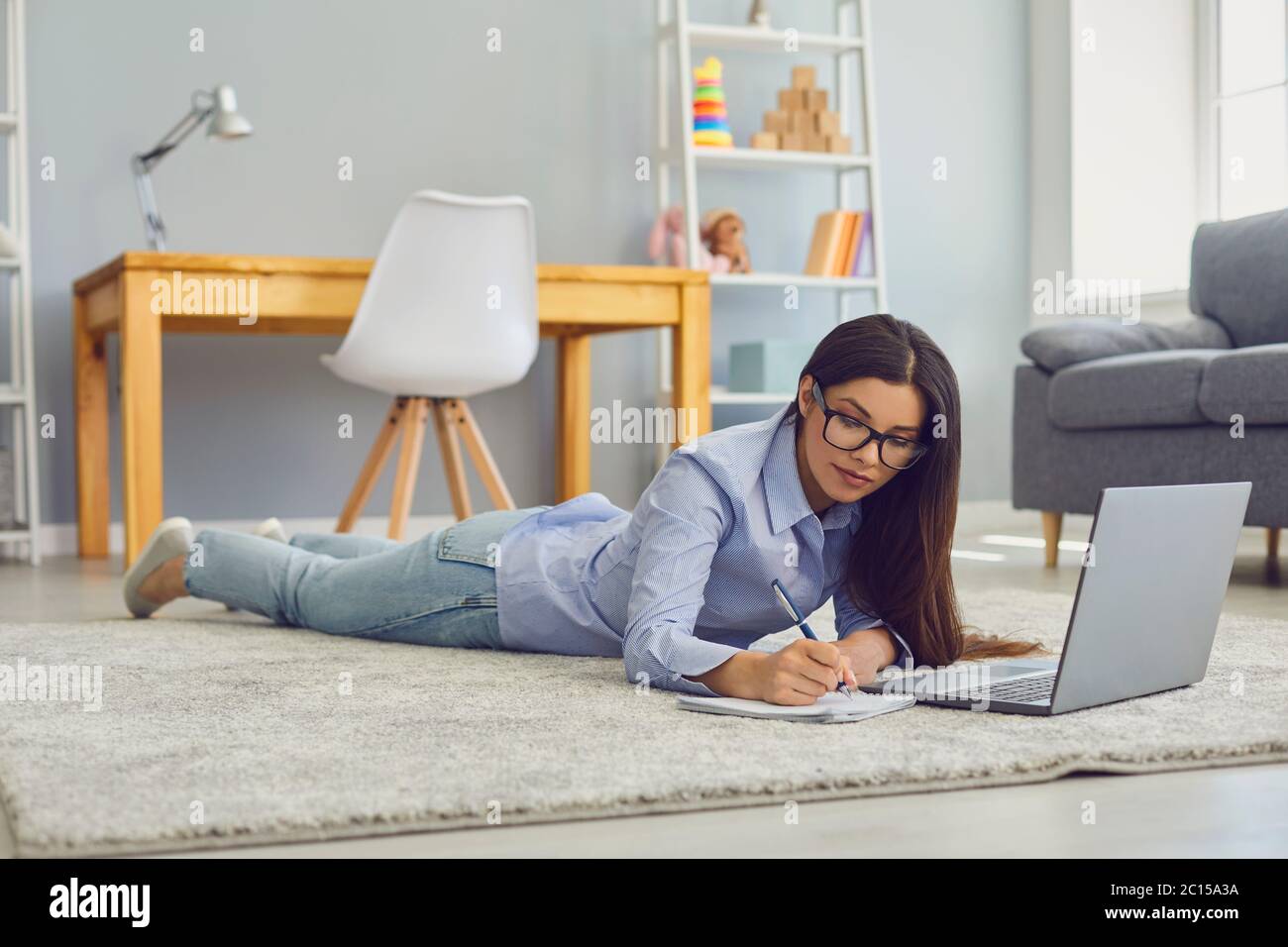 Arbeiten Sie zu Hause. Schöne Frau mit Brille, die sich während einer Online-Geschäftskonferenz oder einer Schulung auf einem Laptop im Zimmer Notizen machen Stockfoto