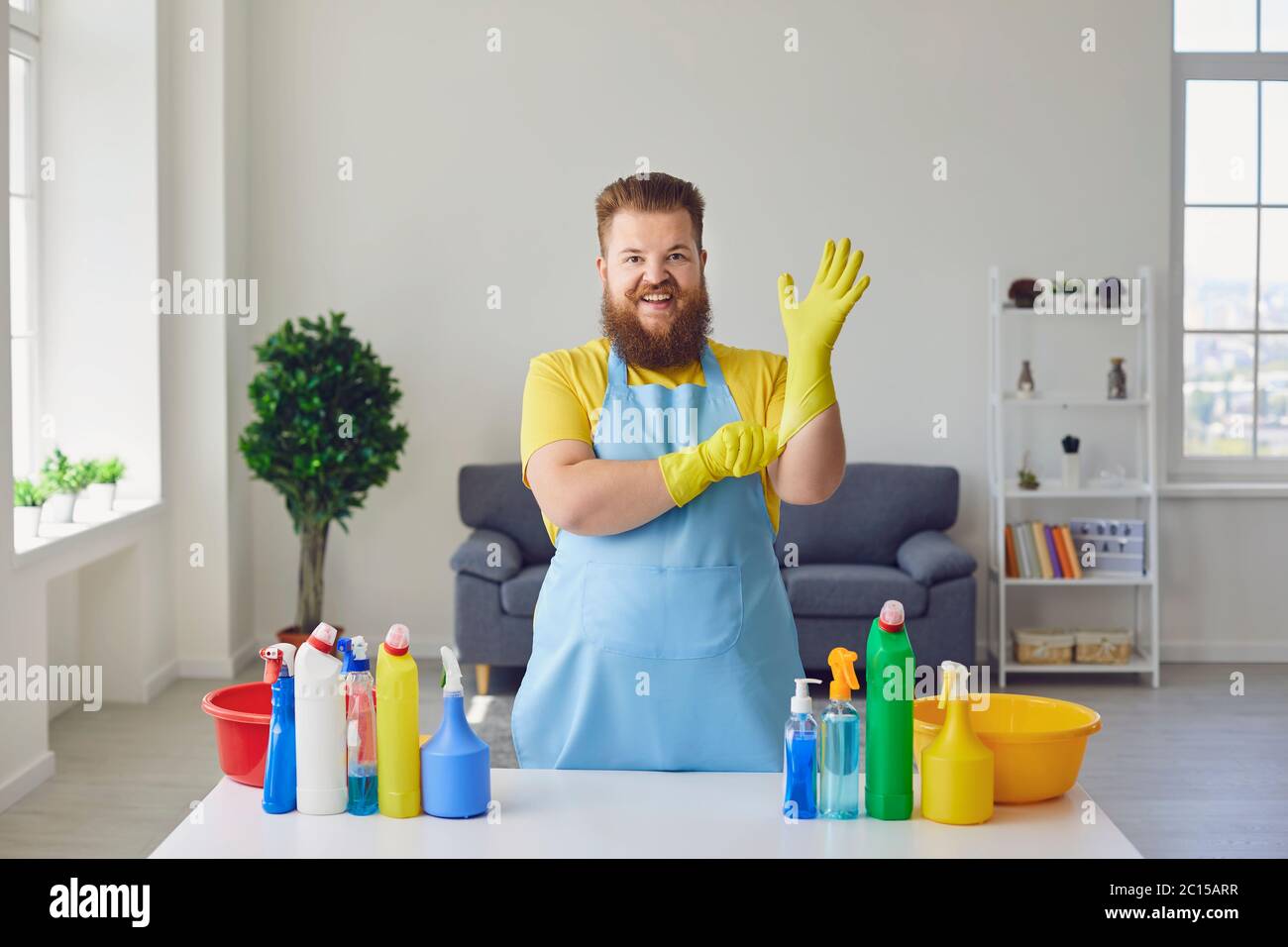 Putzmann im Zimmer. Fröhlicher Mann in Gummihandschuhen mit Reinigungsprodukten zu Hause Stockfoto