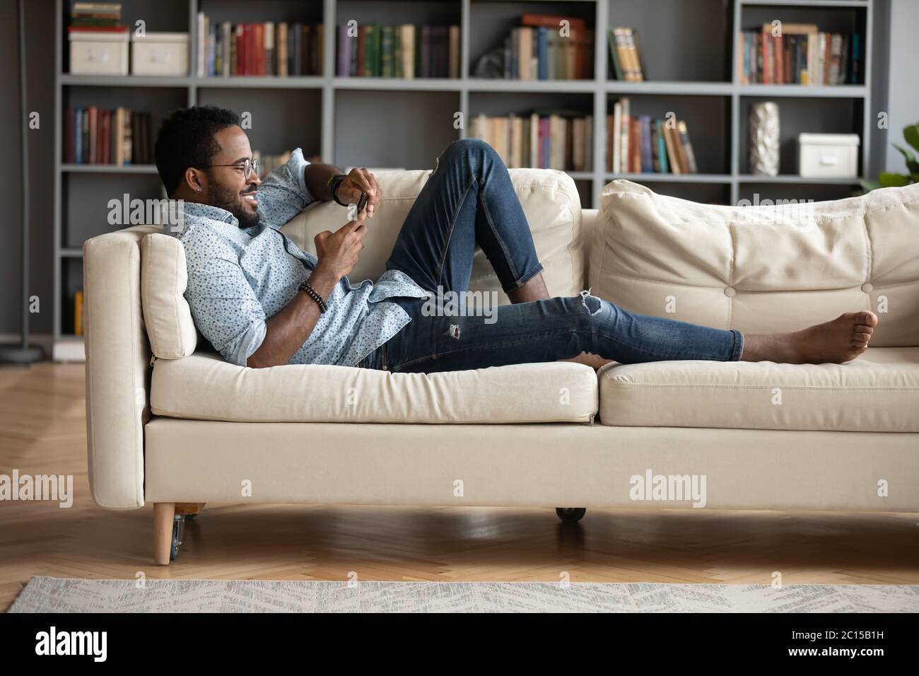 Afrikanischer Kerl liegt auf dem Sofa mit Smartphone-Surfen zu Hause Stockfoto
