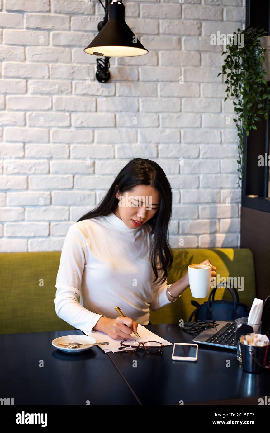 Asiatische Frau arbeitet auf Laptop und mit einem Kaffee in einer Bar. Remote-Arbeit online außerhalb des Büros Stockfoto