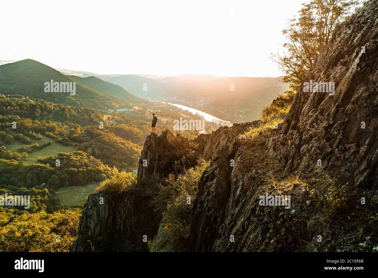 Silhouette der Person auf dem hohen Felsen bei Sonnenuntergang. Wanderer zufrieden genießen Aussicht. Großer Mann auf felsigen Klippen, der die Landschaft beobachtet. Lebendig und stark Stockfoto