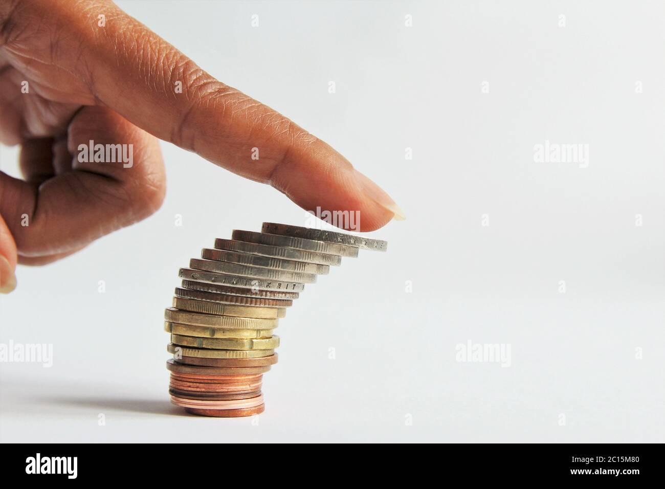 Unterdrückung Konzept, Nahaufnahme Zeigefinger drücken auf den Stapel von Geld Münzen sind im Begriff, nach unten fallen. Foto isolieren auf weißen Seitenansicht Kopieplatz Stockfoto