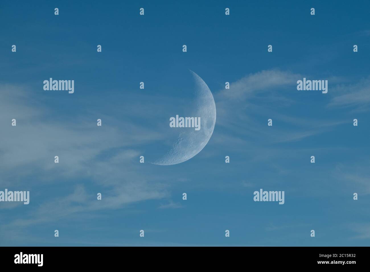 Blauer Himmel mit flüsterigen, straggly Wolken und einem Wachsen oder abnehmenden Halbmond. Stockfoto