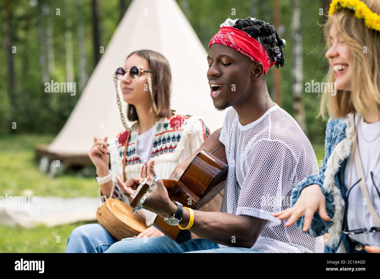 Talentierter junger schwarzer Kerl, der Gitarre spielt und singt, während er mit engen Freunden eine Campingparty genießt Stockfoto