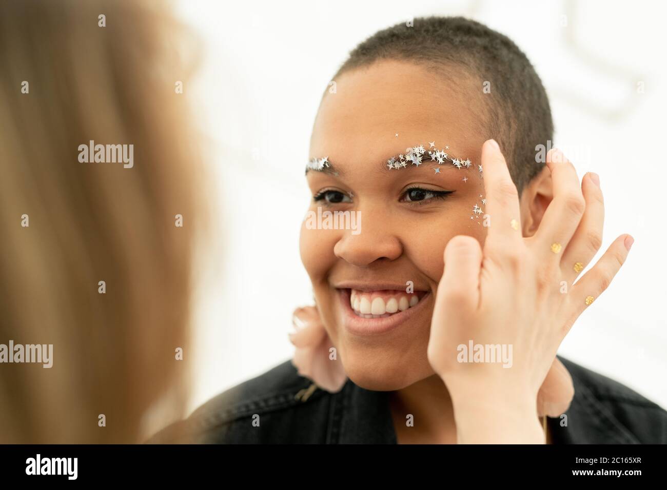 Nahaufnahme der Frau Anwendung Stern Glitzer auf Gesicht der schwarzen Frau, während Make-up zu ihr Stockfoto