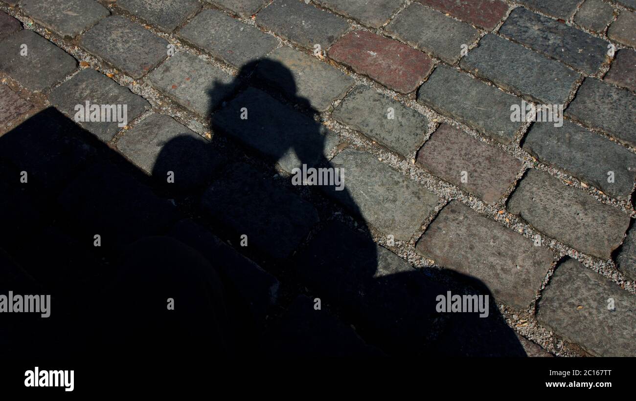 Schwarzer Schatten eines Mannes, der ein projiziertes Foto auf einem Boden aus alten grauen Steinen gemacht hat Stockfoto