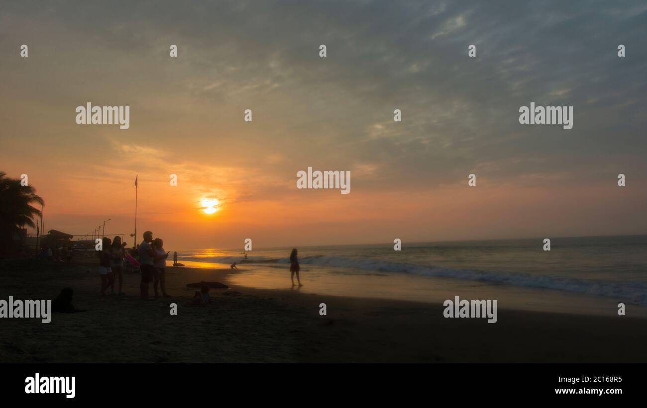 Schwarze Silhouette von Menschen, die am Tonsupa Strand bei einem bewölkten Sonnenuntergang spazieren. Esmeraldas - Ecuador Stockfoto