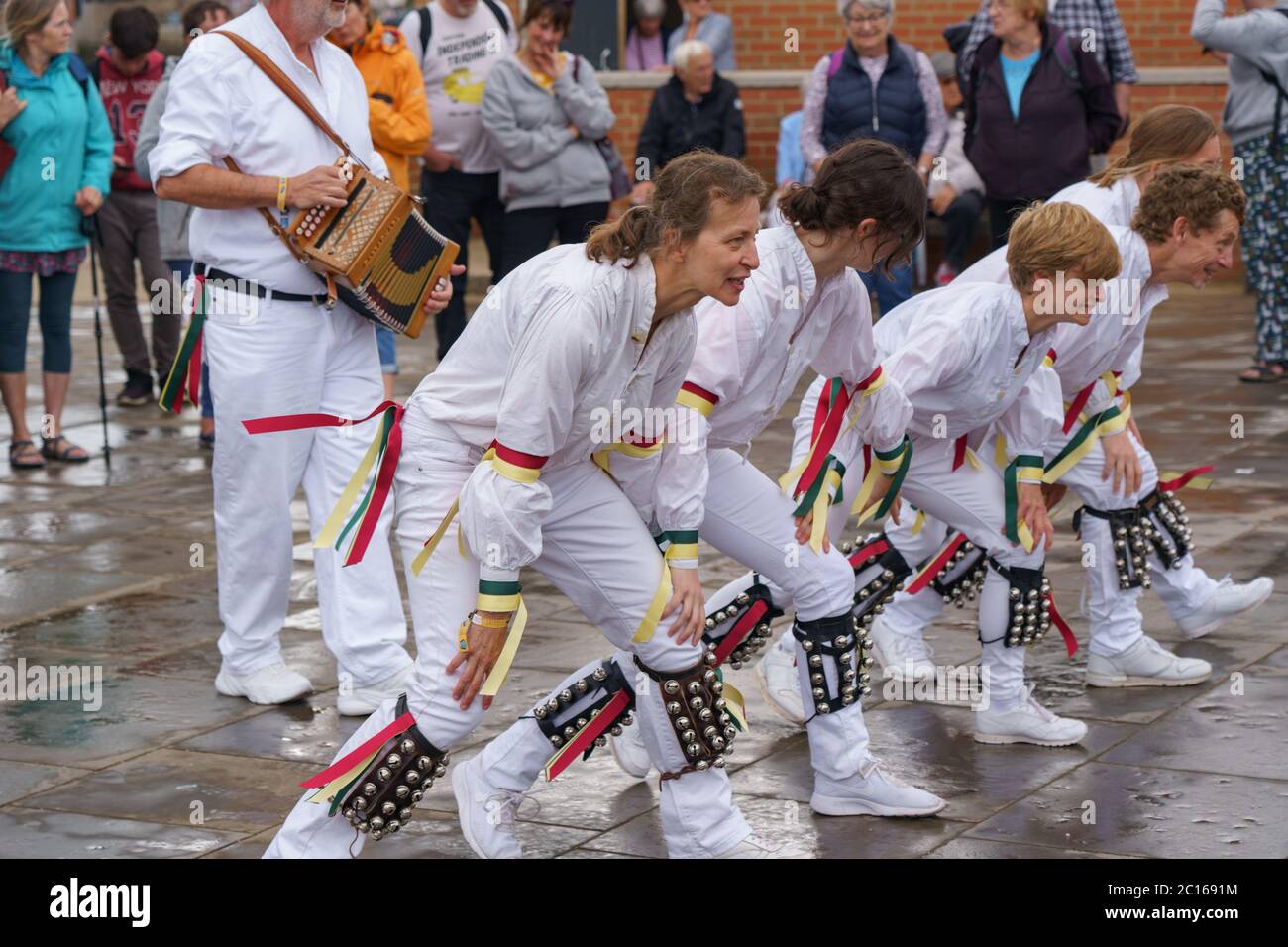 Morris-Tänzer, die in weiß gekleidet sind und Knieglocken und farbige Bänder tragen, tanzen an der Strandpromenade der Folk Week in Whitby, North Yorkshire, Großbritannien. Stockfoto