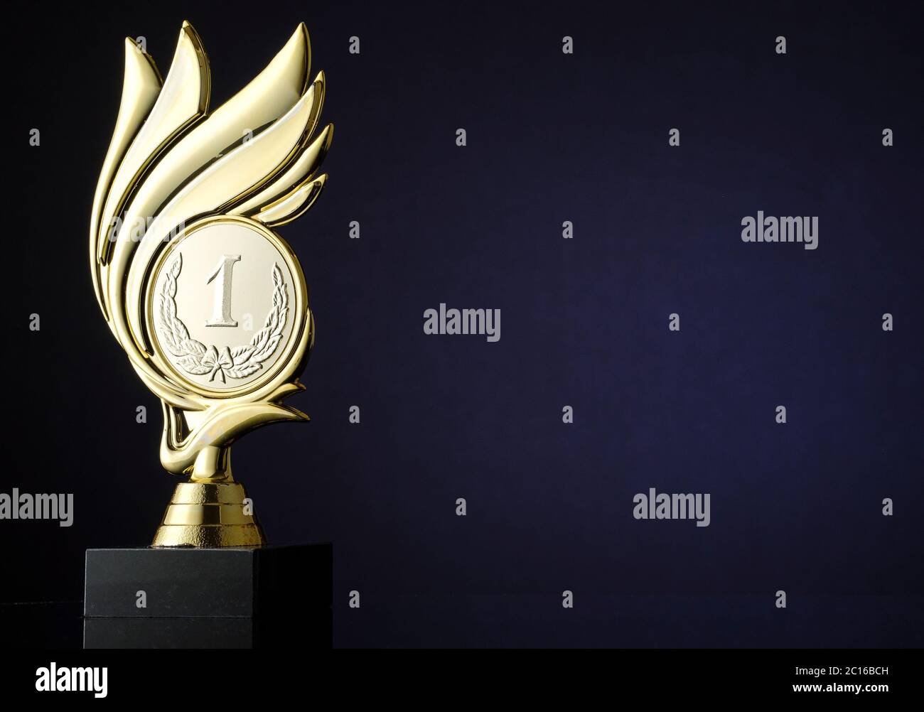 Gewinner Goldtrophäe mit gravierter Medaillon mit Nummer 1 und Lorbeerkranz umgeben von einem Wirbel über einem dunkelblauen Hintergrund mit Copyspace für einen cha Stockfoto