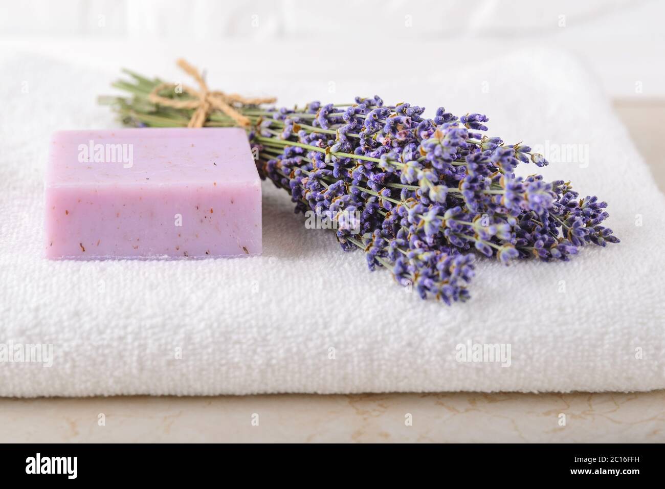 Frisch duftender Lavendel und lila Lavendelseife auf einem weißen Frottee-Handtuch im Badezimmer. Hausgemachtes Spa, Hautpflege und Kosmetologie Konzept. Vorderansicht. Stockfoto