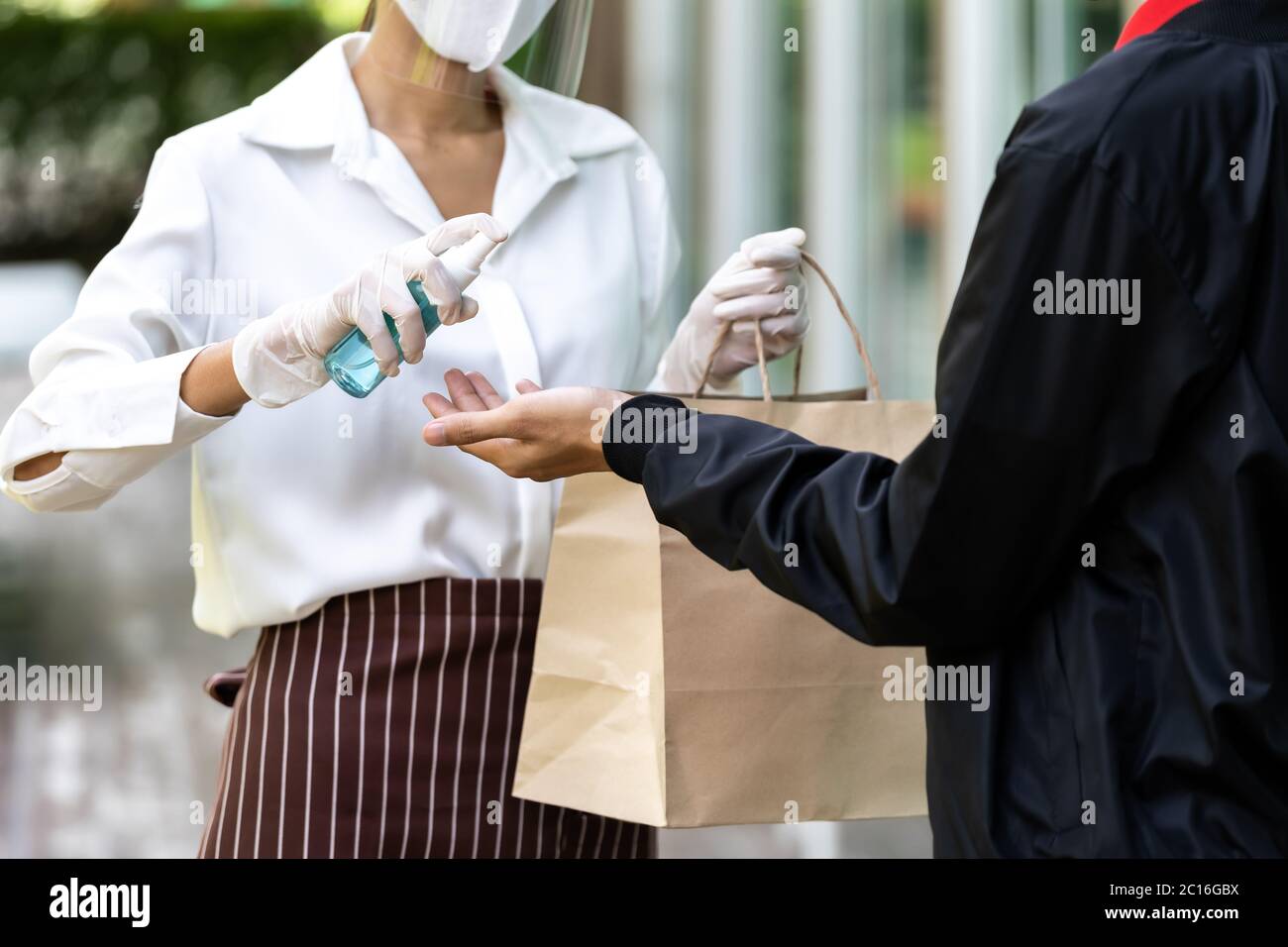 Kellnerin sprüht Alocohol auf der Hand der lieferly Mann vor geben Bäckerei Lebensmittelbeutel für die Reinigung und Hygiene als neue normale für Lebensmittel Lieferdienst w Stockfoto