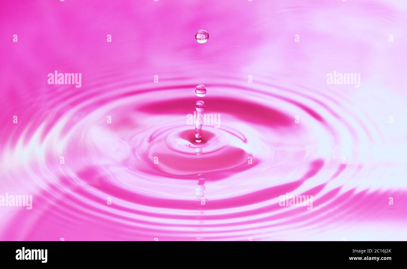 Wassertropfen fallen ins Wasser und bilden perfekte konzentrische Kreise. Abstrakter rosa Hintergrund. Stockfoto