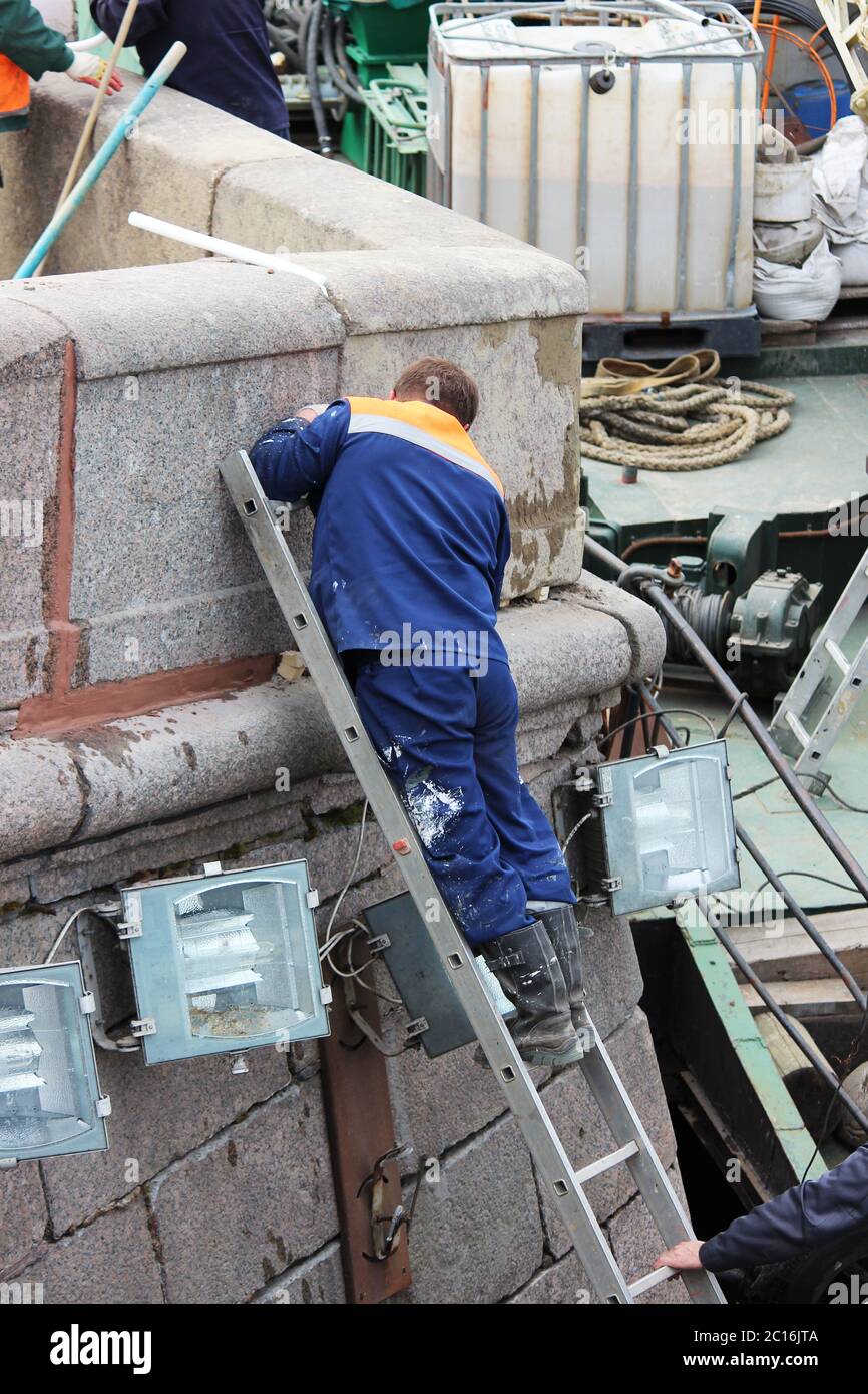 Der Maurer repariert die Nahten zwischen den Granitplatten am Ufer des Flusses Fontanka in St. Petersburg Stockfoto