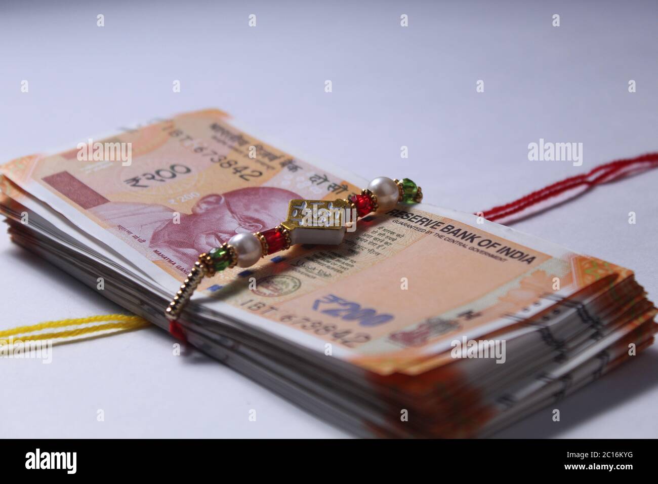 Raksha Bandhan Festivalkonzept mit dem Designer Rakhi oder Wrist Band Mit vereinzeltem Reis und Kumkum, mit indischer Währung über bunt platziert Stockfoto