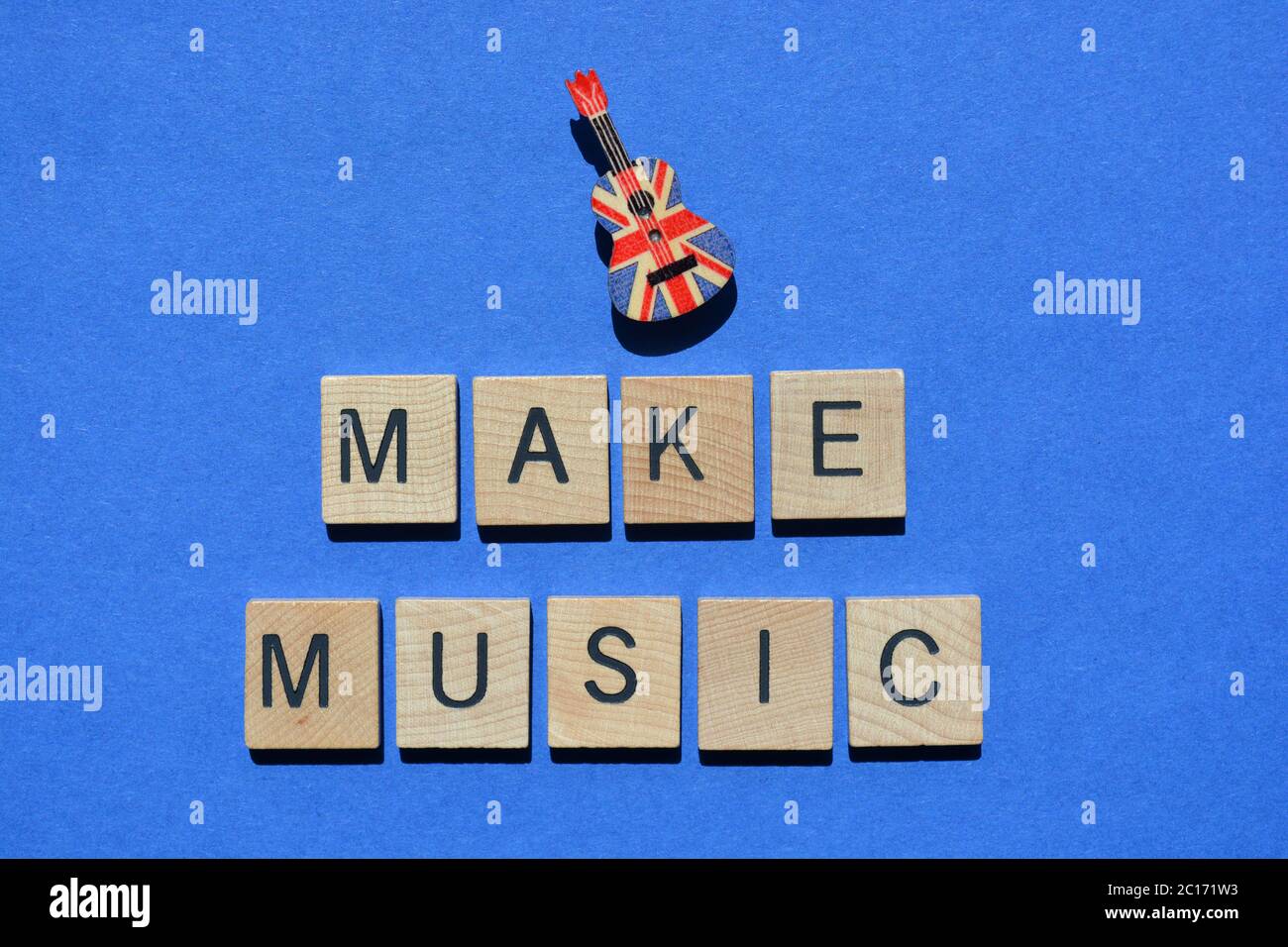 Make Music, Wörter in 3d-Holz-Alphabet Buchstaben isoliert auf blauem Hintergrund, mit einem Ukulele-Stift mit einem Union Jack Flag-Muster verziert Stockfoto