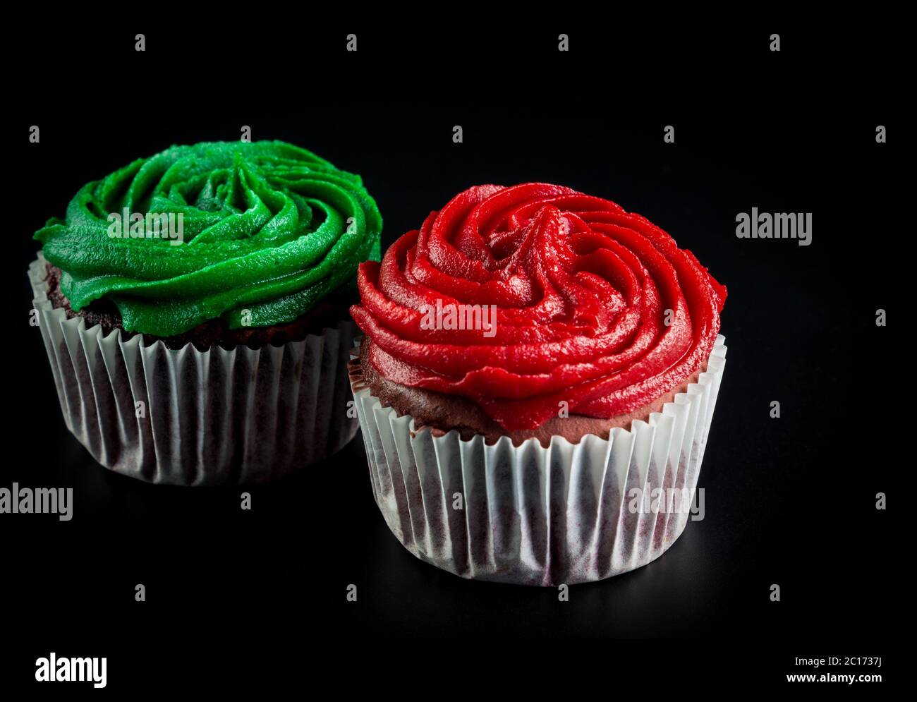 Zwei Muffins, rot und grün auf schwarzem Hintergrund isoliert Stockfoto