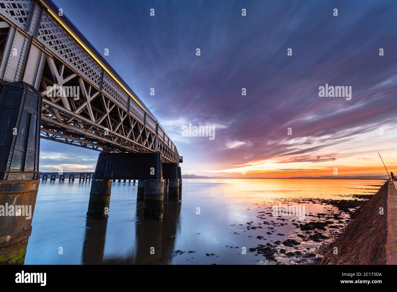 Sonnenuntergang und die Tay Rail Bridge, als ein Zug vorbeifährt, Dundee, Schottland, Vereinigtes Königreich. Stockfoto