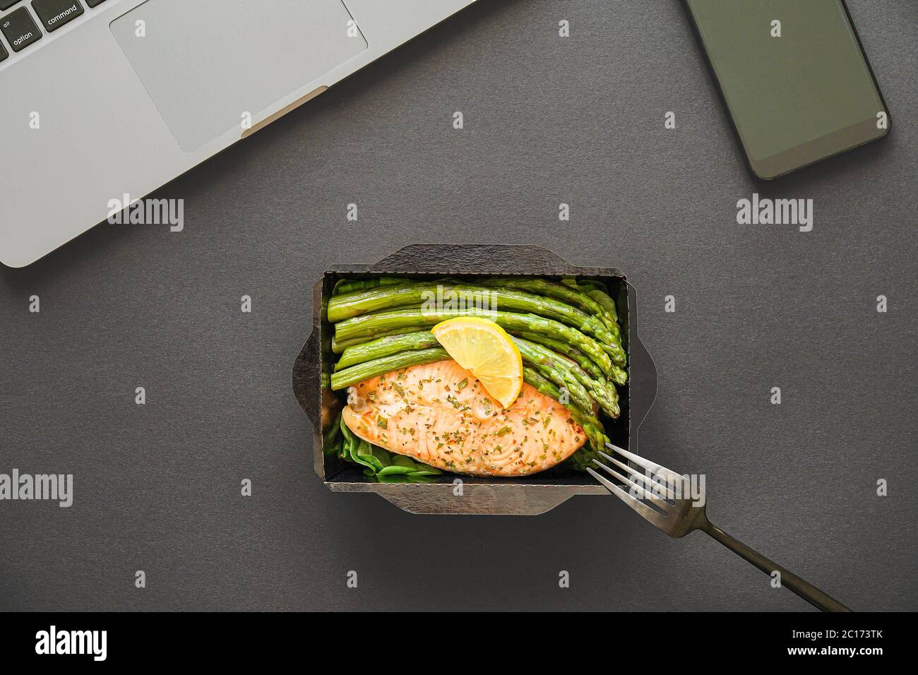 Büro Lebensmittel Lieferung Mahlzeit Fisch und Gemüse Lunchbox bei der Arbeit auf schwarzem Tisch. Stockfoto