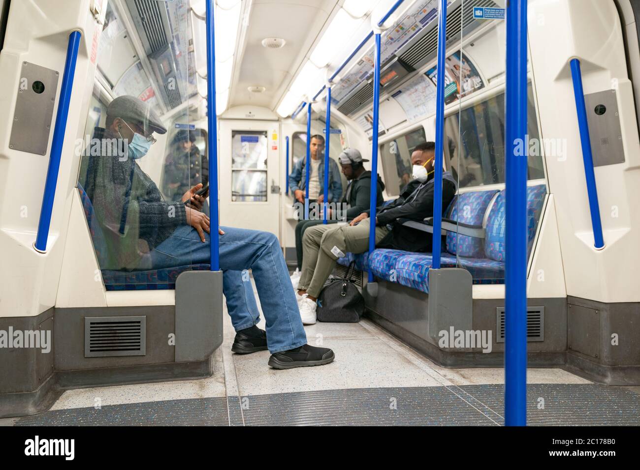 LONDON, ENGLAND - 8. JUNI 2020: Gruppe von Männern auf einer Piccadilly Line London Underground Train Carriage mit Gesichtsmasken während der COVID-19 Pandemie 4 Stockfoto