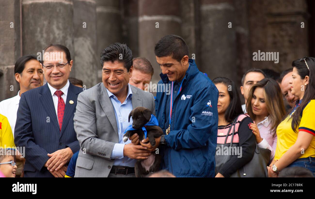 Quito, Pichincha / Ecuador - Juni 11 2019: Richard Carapaz, der Sieger des Giro d'Italia 2019, erhält einen schwarzen Welpen vom Bürgermeister Jorge Yu Stockfoto