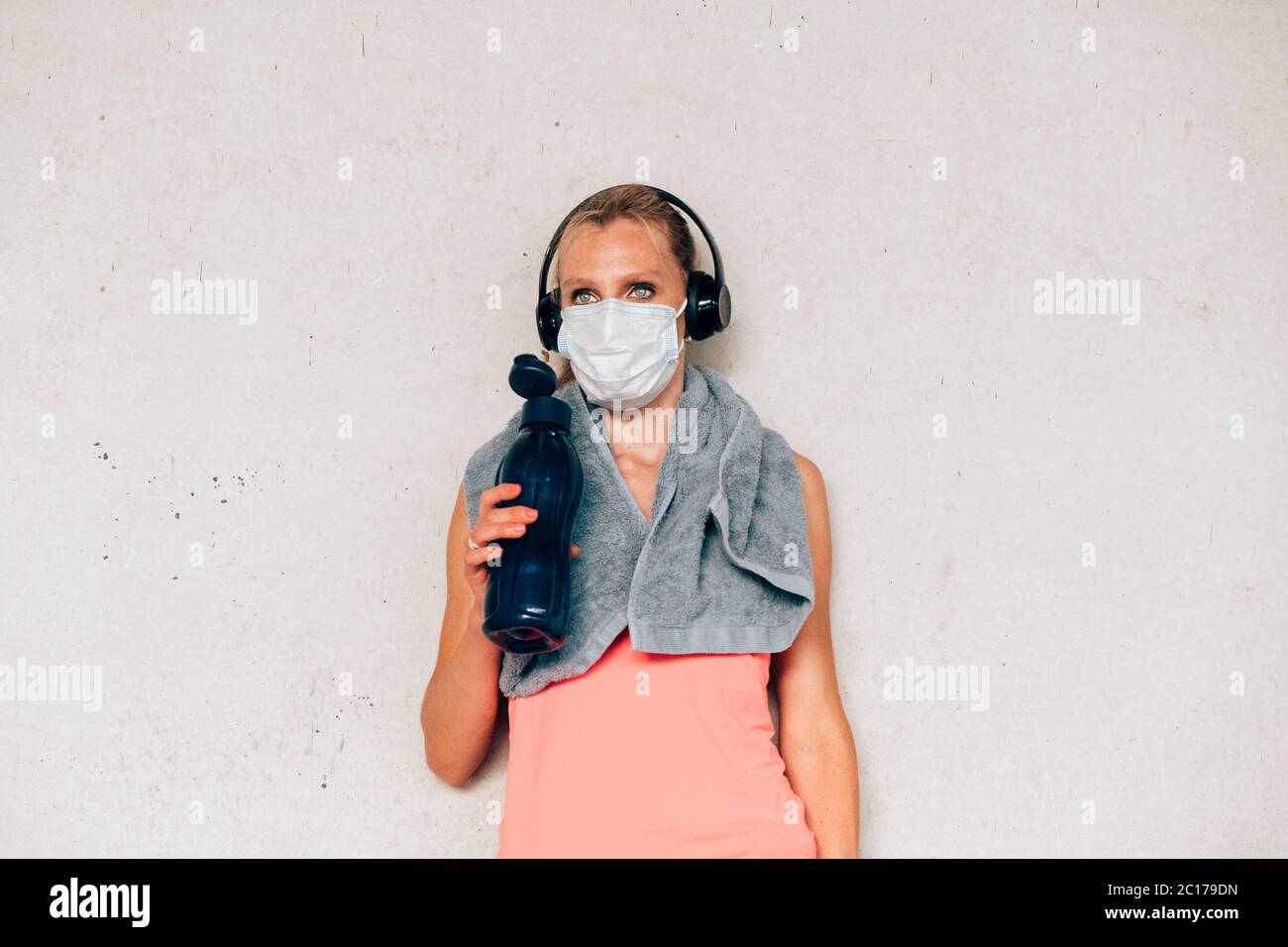 Fitness Frau mit Schutzmaske an einer Wand im Laufseil stehend. Frau, die sich nach dem Arbeiten auf konkreten Hintergrund ausruhen. Stockfoto