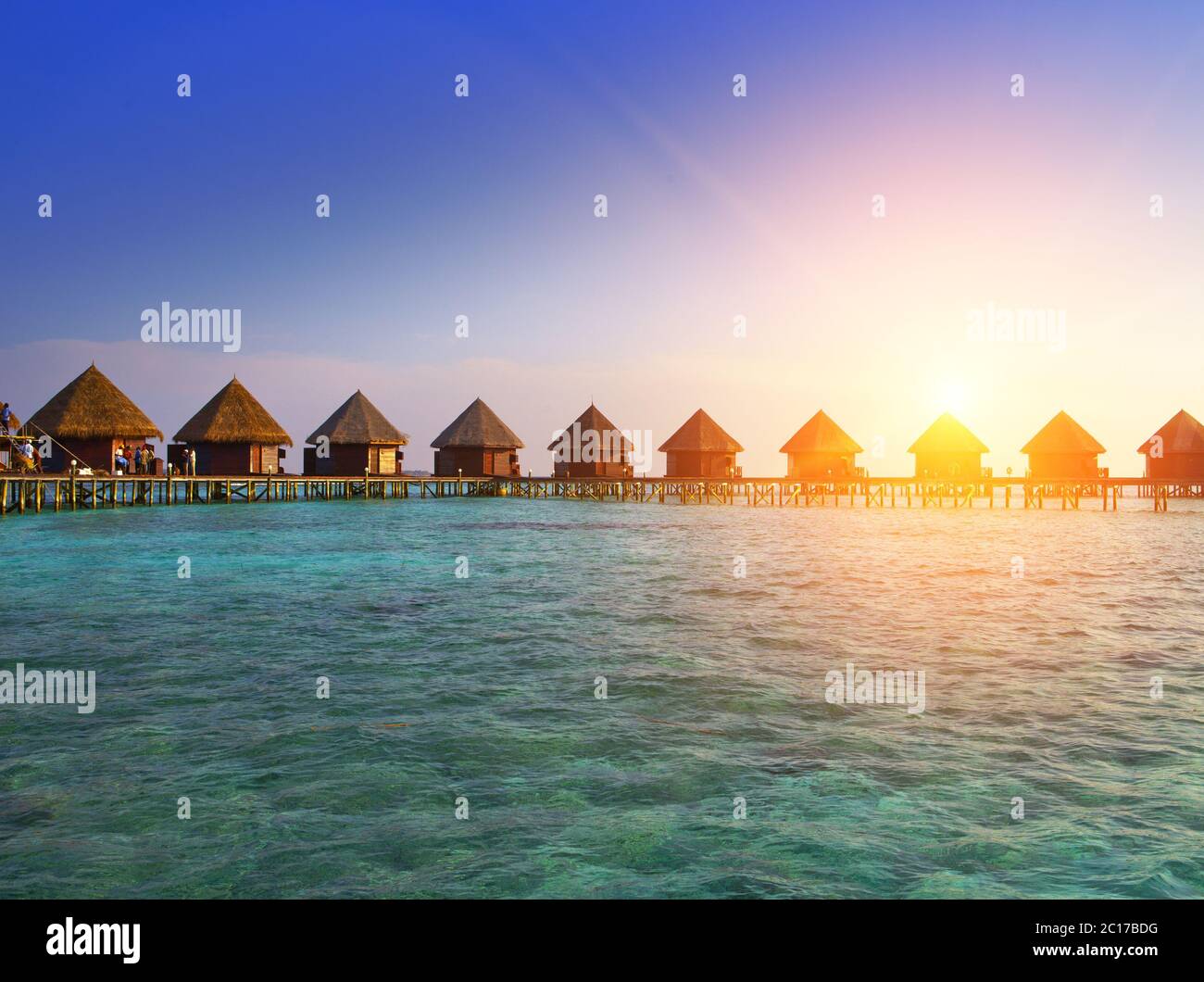 Häuser über die Transparente ruhigen Meer Wasser auf einen Sonnenuntergang. Malediven Stockfoto