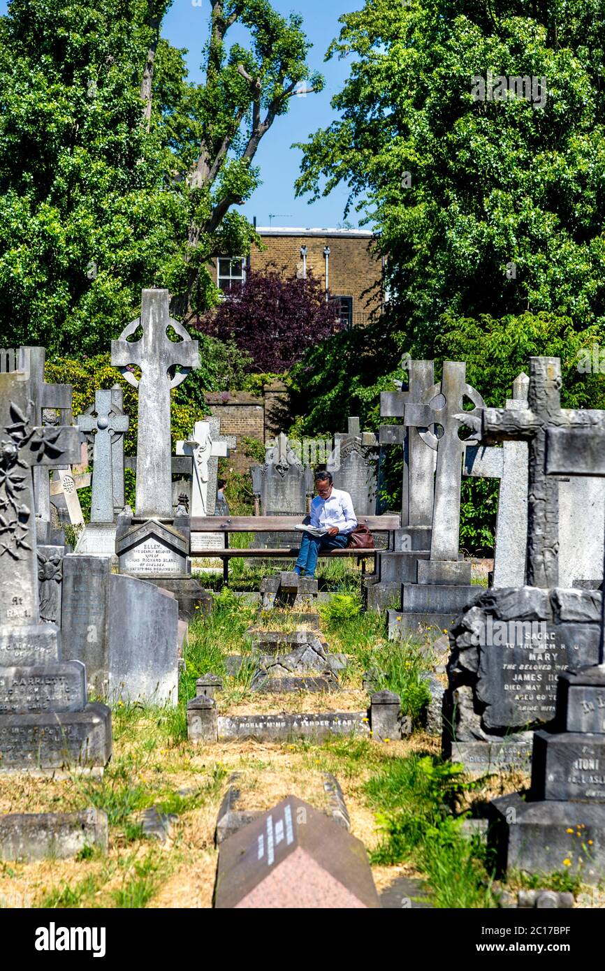 Mann auf einer Bank sitzend, Zeitung lesen, Brompton Cemetery, London, Großbritannien Stockfoto