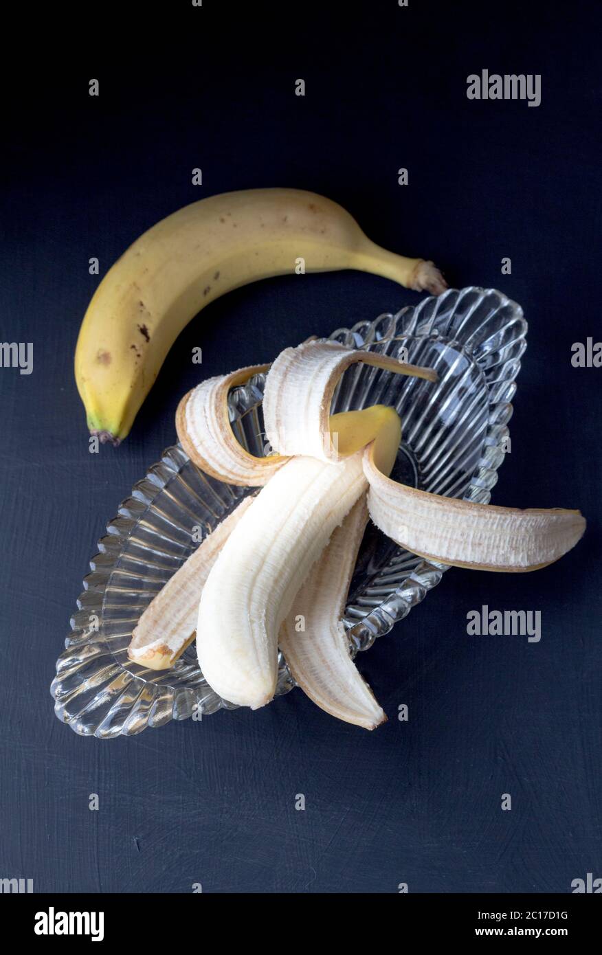 Banane in Glas geschält Banane Split antike Schüssel mit selektivem Fokus und eine ungeschält auf schwarzem Rücken Stockfoto