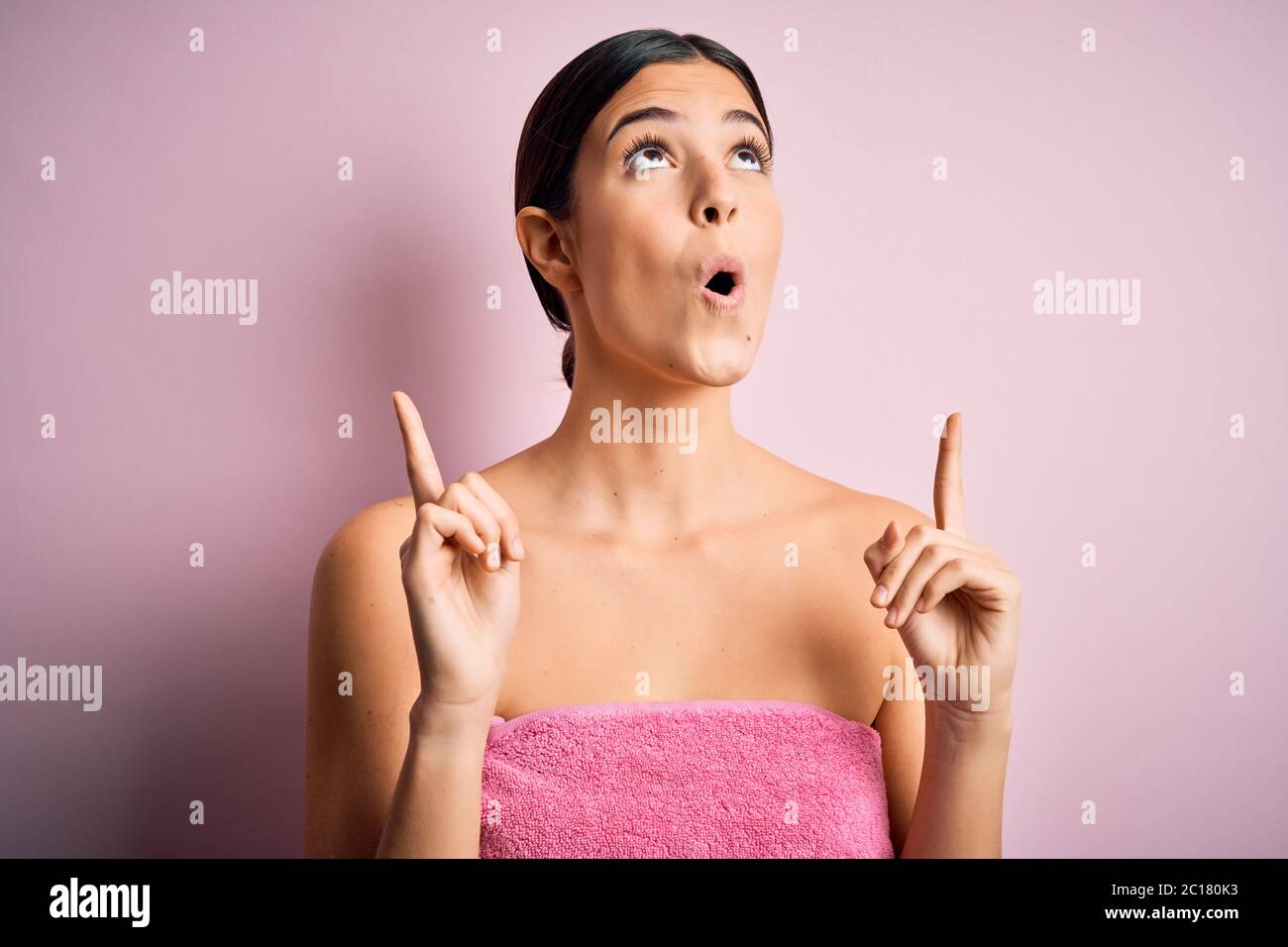 Junge schöne Mädchen tragen Handtuch Dusche nach Bad stehen über isoliert  rosa Hintergrund erstaunt und überrascht suchen nach oben und zeigt mit den  Fingern Stockfotografie - Alamy
