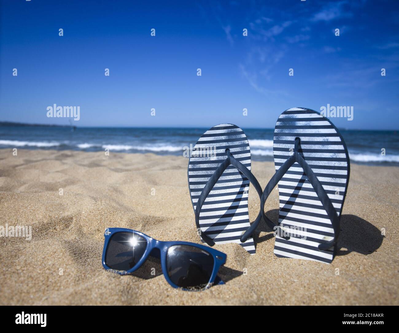 Blauer Sandalflip und Sonnenbrille am Sandstrand mit blauem Meer und Himmel Hintergrund in Sommerferien. Speicherplatz kopieren Stockfoto