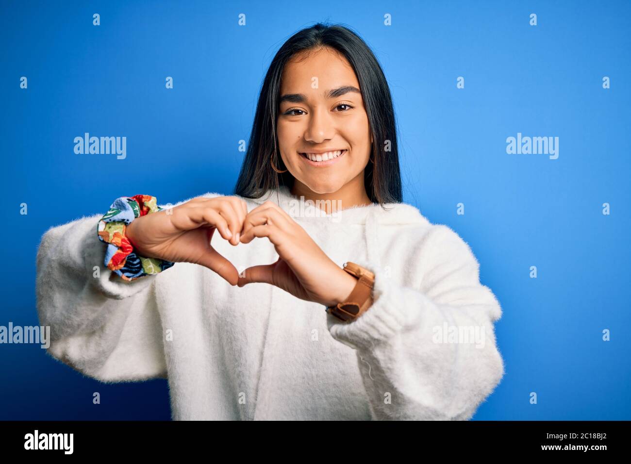 Junge schöne asiatische Sportlerin trägt Sweatshirt über isoliert blauen Hintergrund lächelnd in der Liebe zeigt Herz Symbol und Form mit Händen. Stockfoto