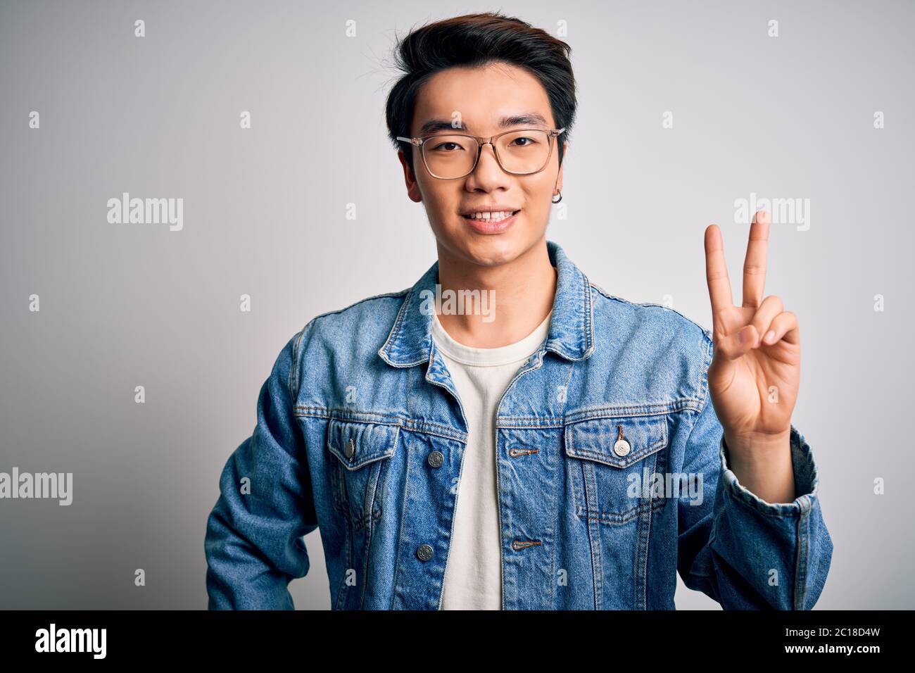 Junger hübscher chinese, der Jeanjacke und Brille auf weißem Hintergrund  trägt und mit den Fingern Nummer zwei zeigt und zeigt, während er sich  angibt Stockfotografie - Alamy