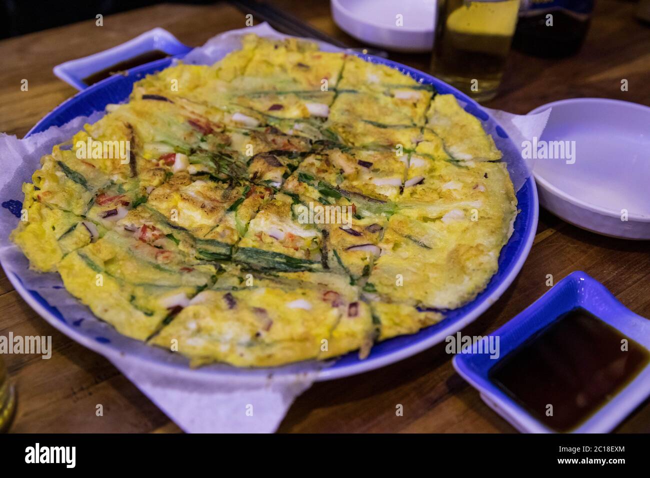 Koreanische herzhafte Tintenfische, Garnelen Meeresfrüchte und Schalotten Pfannkuchen, Pajeon, auf einem großen Teller in einem Restaurant mit Dip-Sauce. Stockfoto