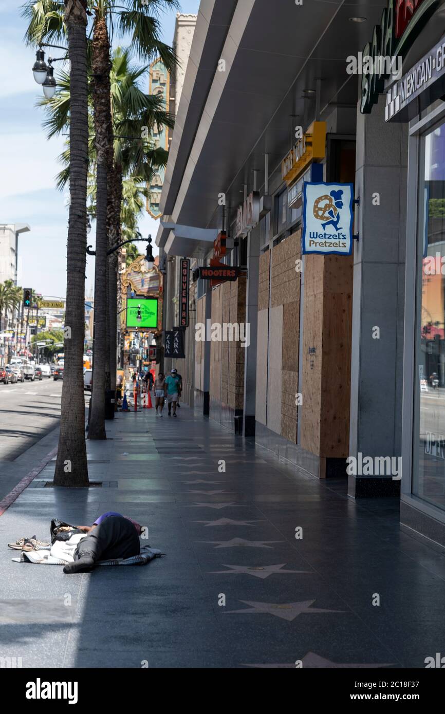 Hollywood, CA/USA - 8. Juni 2020: Eine obdachlose Frau schläft auf dem Hollywood Walk of Fame neben Unternehmen, die nach einer Reihe von Black Lives in die Läden gehen Stockfoto