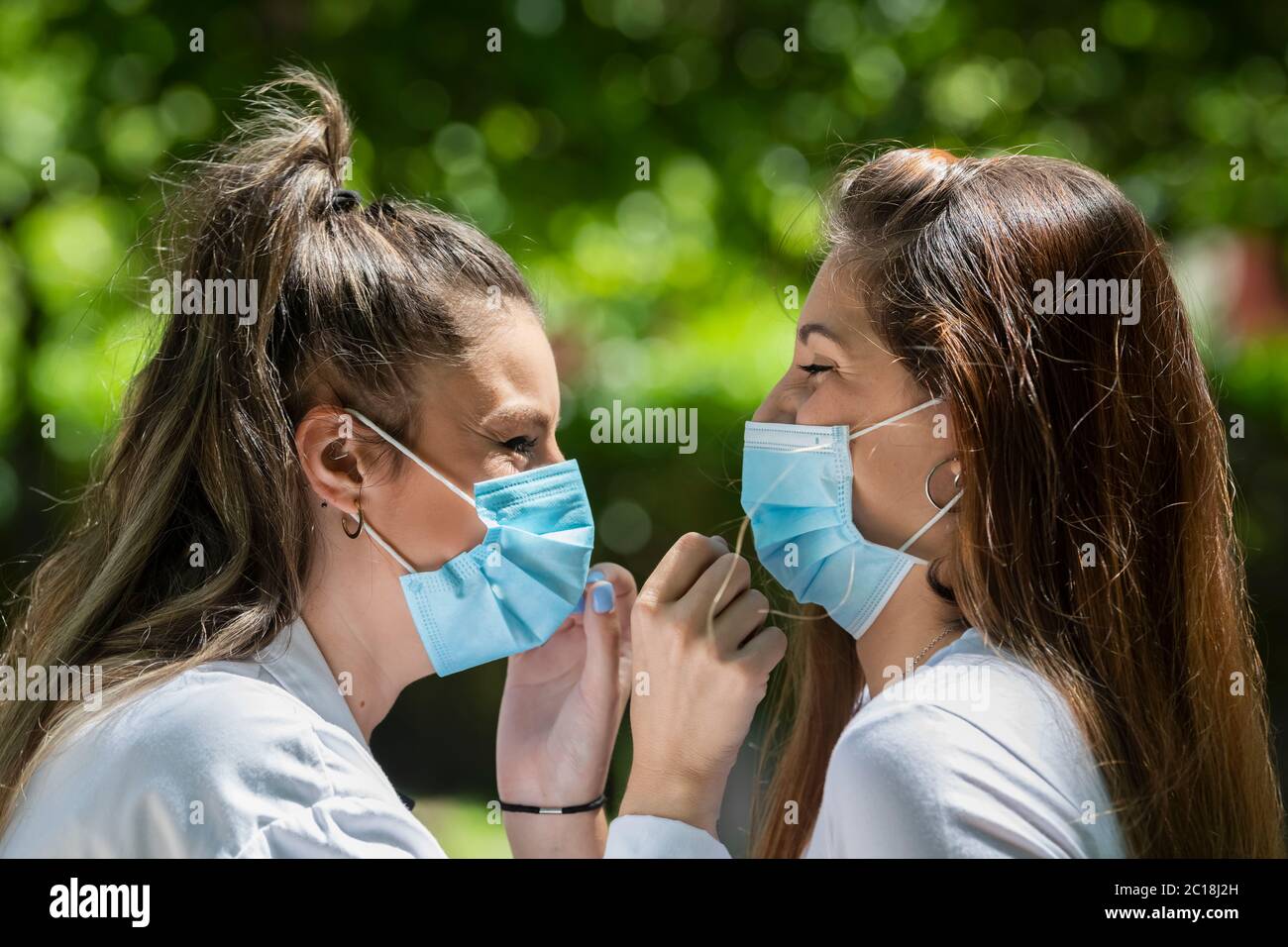 Nahaufnahme von zwei jungen Frauen, die chirurgische Masken tragen und sich gegenseitig anlächeln, auf einem unfokussierten Hintergrund. Neues Lifestyle- und Sicherheitskonzept. Stockfoto