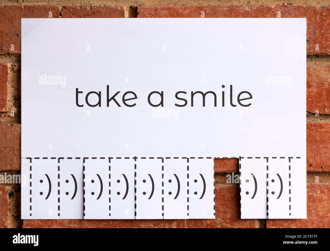 Ein Papier mit dem Satz "Take a Smile" geschrieben mit verschiedenen Stücken mit lächelnden Gesichtern abzureißen. Lächeln ist frei. Das Bild ist von vorne. Stockfoto
