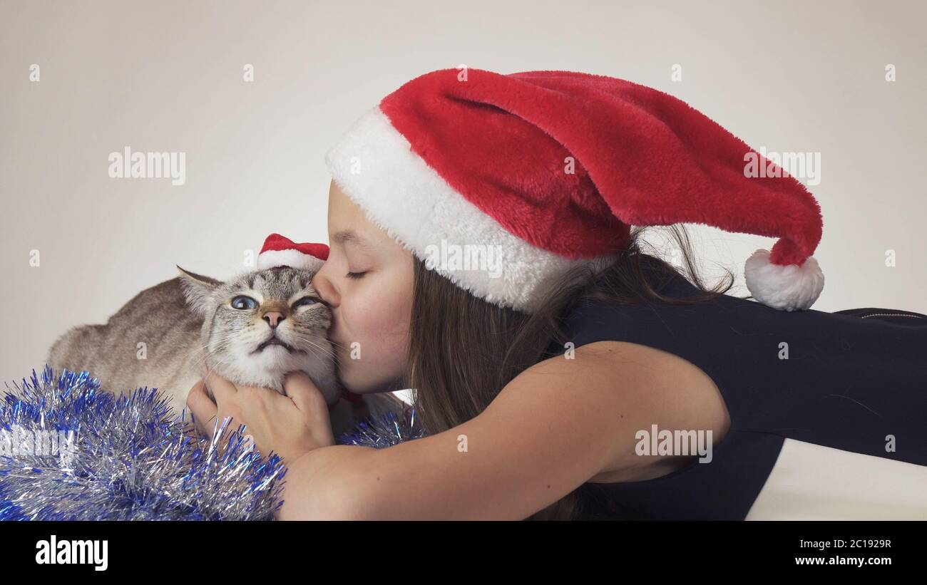 Schöne Teenager-Mädchen und ihre Katze in Santa Claus Kappen freudig küssen auf weißem Hintergrund Stockfoto