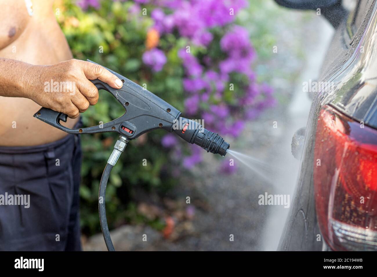 Manuelle Autowäsche mit unter Druck stehendem Wasser im Freien. Mann, der das Auto mit Hochdruckwasser auf einer Straße putzt. Stockfoto