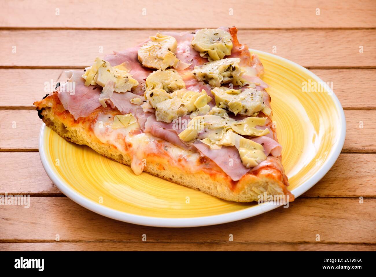 Italienische Pizza in Scheiben mit Schinken und Artischocken, gewürzt auf einem weißen Teller auf einem Holztisch Stockfoto