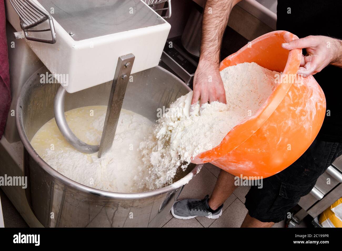 Koch Zugabe von Mehl zu einem kommerziellen Mixer während der Vorbereitung einer Partie Pizzateig in einer Pizzeria in der Nähe auf seine Hände Stockfoto