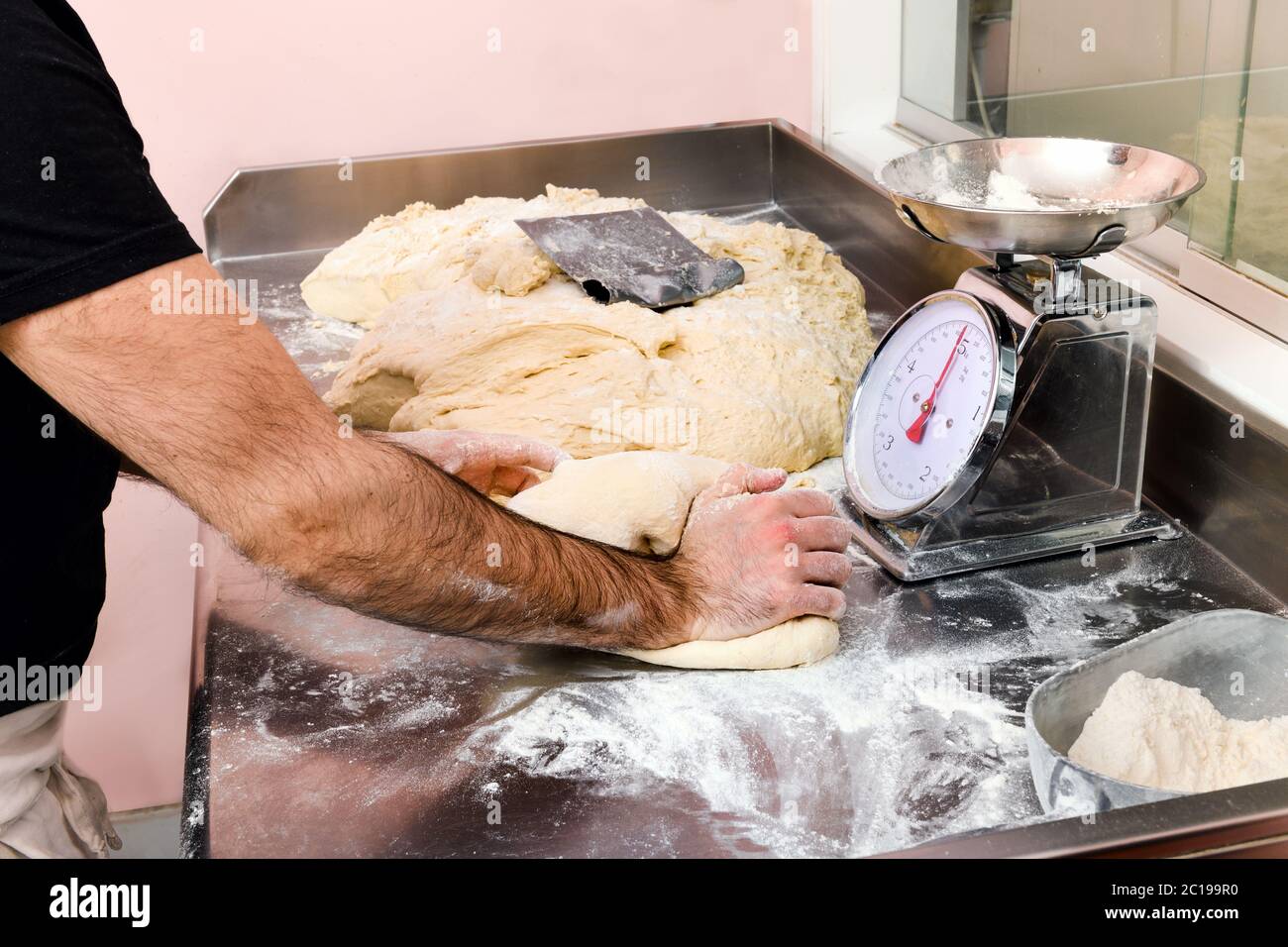 Koch knetet eine Charge frischen Pizzateig in einem Restaurant oder einer Pizzeria auf einer bemehlten Theke mit Küchenwaage Stockfoto