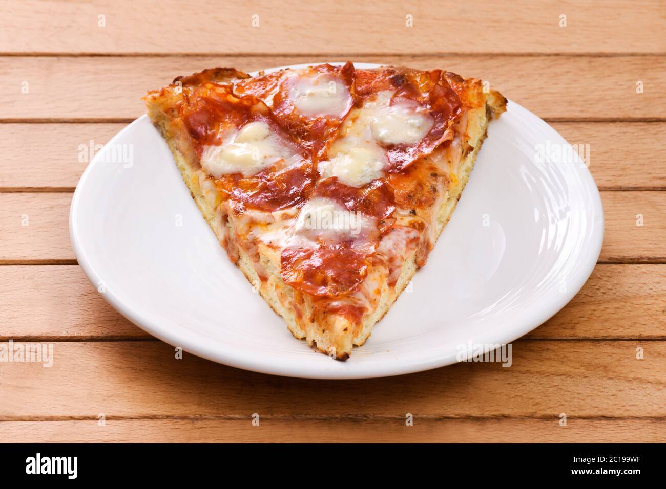 Ein Stück italienische Salami-Pizza mit würzigem Gorgonzola-Käse auf einem weißen Teller auf einem Holztisch serviert Stockfoto