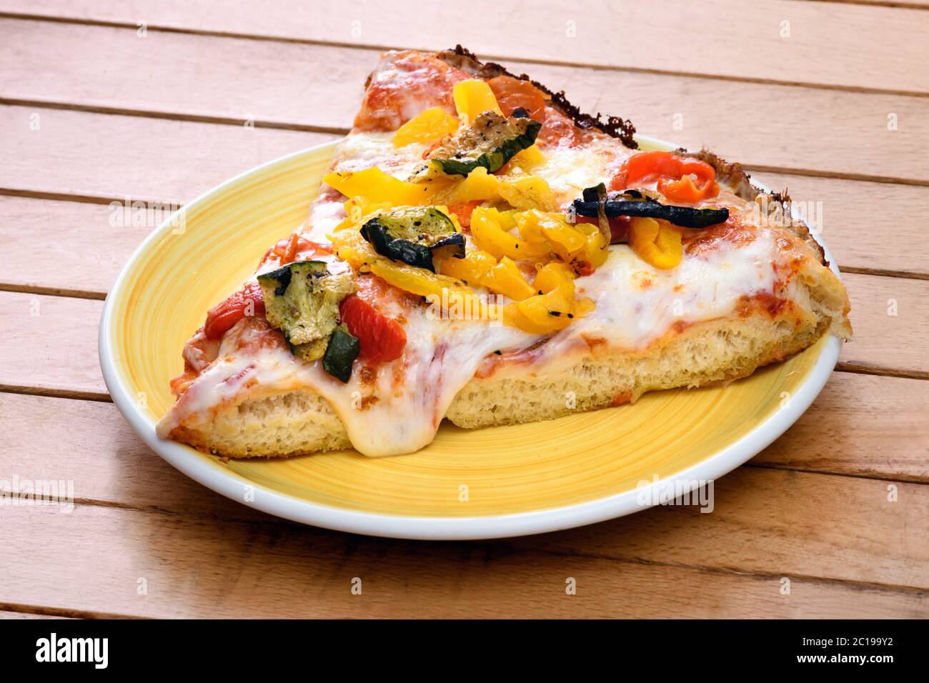 Ein Stück traditionelle italienische Pizza mit gegrilltem Gemüse Belag auf geschmolzenem Mozzarella-Käse serviert auf einem gelben Teller auf einem Holztisch Stockfoto