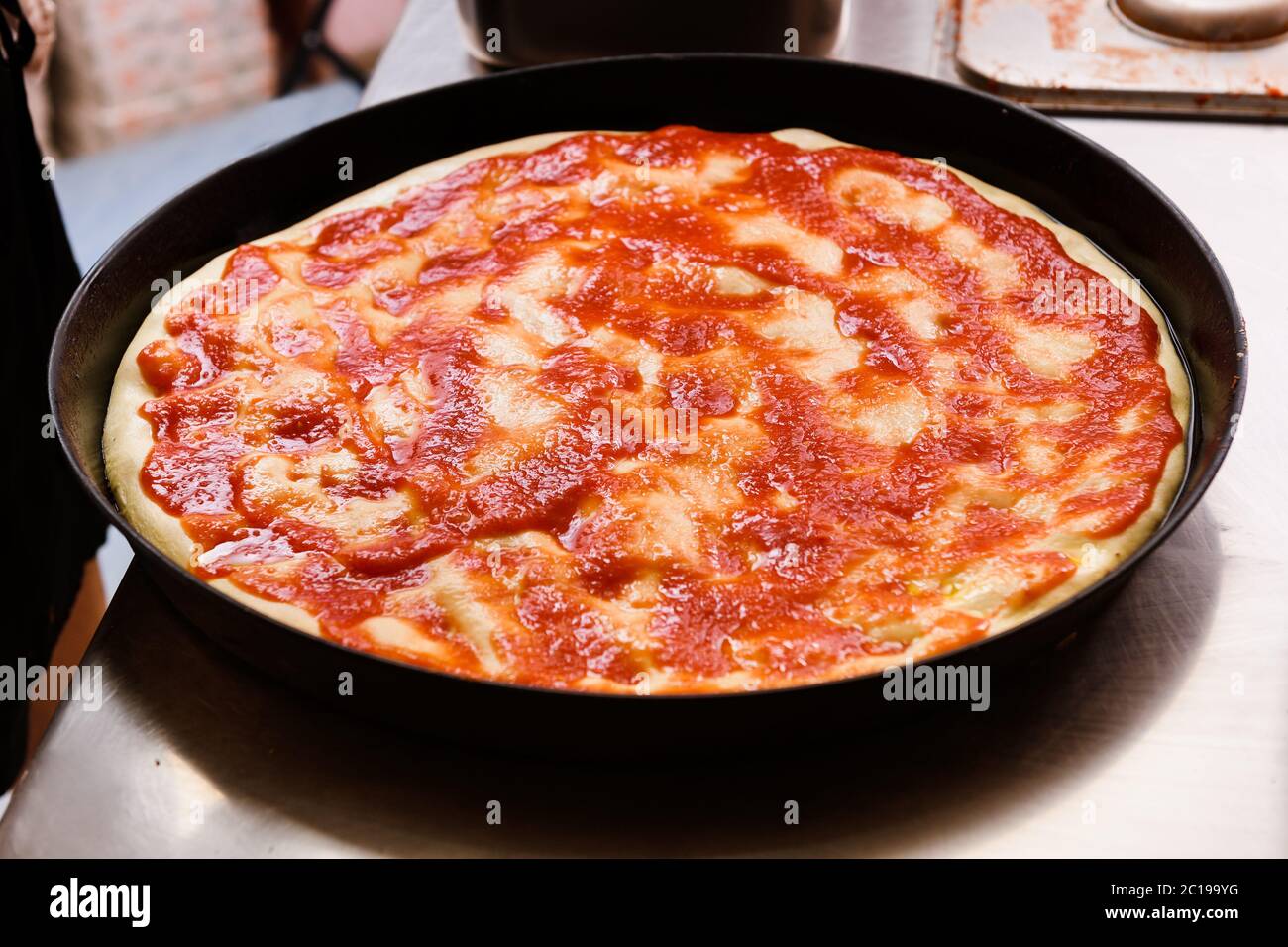 Pizza mit Tomatenmark in einem Backblech bereit für den Ofen in der Nähe in einer Restaurantküche Stockfoto