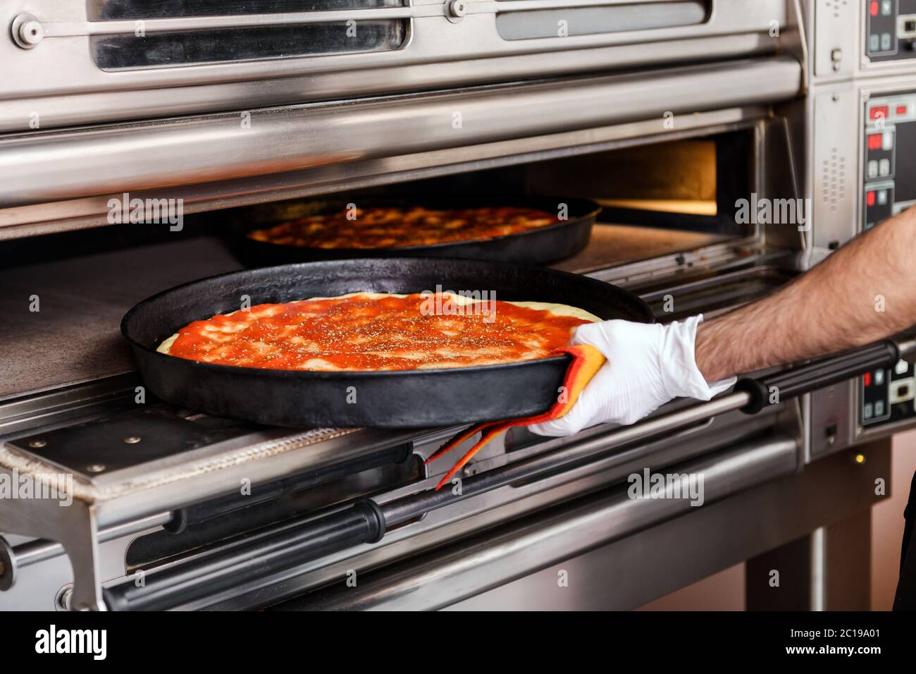 Koch platziert eine Pizza auf einem Backblech in einen Ofen in einer Pizzeria oder Restaurant in einer Nahaufnahme auf seine Hand und das Essen Stockfoto